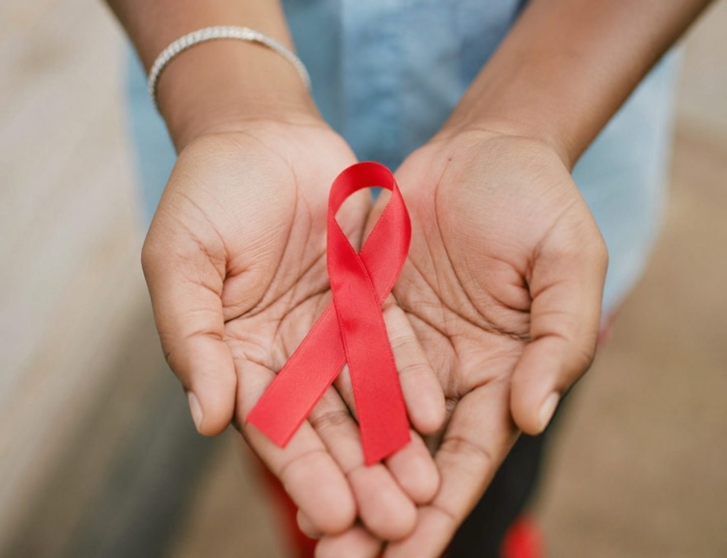 HIV/AIDS awareness ribbon held by supportive hands